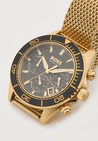 Ρολόι χειρός Hugo Boss σε χρυσό τόνο με μαύρο καντράν, τρεις υποκαντράν, ένδειξη ημερομηνίας, περιστρεφόμενο στεφάνι και μπρασελέ από μεταλλικό δίχτυ.