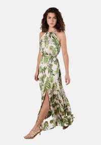 Maxikleid aus leichtem Stoff mit grünem Blattmuster, Neckholder-Ausschnitt, tailliertem Bund und Schlitz bis zur Oberschenkelhöhe. Kombiniert mit nudefarbenen Riemchenheels.