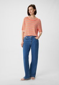 Paski krótki rękaw w pomarańczowym i białym kolorze, noszony z niebieskimi spodniami z szerokimi nogawkami na wysoki stan i białymi sandałami.