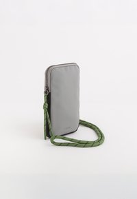 Sac en nylon gris en bandoulière avec une sangle en cordon à motifs verts, fermeture éclair et un petit logo embossé à l'avant. Forme rectangulaire compacte.