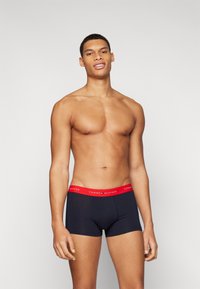 Tengerészek színű boxer alsónemű, piros Tommy Hilfiger gumis derékkal. Az anyag sima tapintású, a gumis derékpánton a márka felirata található.