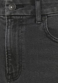 Tejido de mezclilla negra de pantalones, con un cierre visible de botón y cremallera, con un diseño clásico de cinco bolsillos y detalles de costura diagonal.