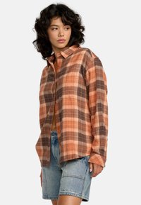 Chemise à carreaux dans des tons orange et marron, avec un devant à boutons, des manches longues et une coupe décontractée, associée à un short en denim.