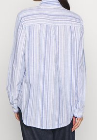 Camicia a maniche lunghe realizzata in tessuto leggero, con strisce verticali blu e bianche, polsini con bottoni e orlo arrotondato.