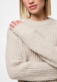Licht beige gebreide trui met een gestructureerd patroon, ribgebreide manchetten en een ronde halslijn. Lange mouwen met een losse pasvorm rond de armen.