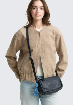 Tanfarbener Wollmischung-Bomberjacke mit Druckknöpfen und gerafftem Bund, kombiniert mit einer kleinen marineblauen strukturierten Crossbody-Tasche, die einen blauen Quastenanhänger hat.