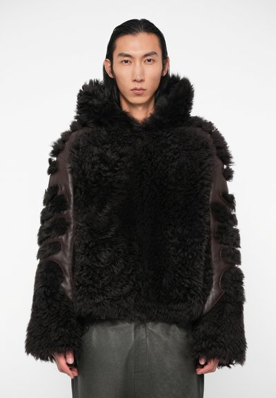 Veste en shearling marron avec un extérieur texturé et duveteux et des accents en cuir ; dispose d'une capuche et de découpes sur les manches.