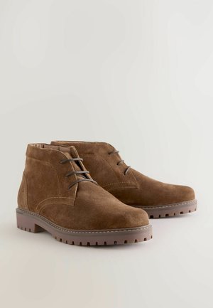 Braune Wildleder-Stiefeletten mit abgerundeter Spitze, Schnürdesign und Gummisohle mit strukturiertem Profil für besseren Halt.