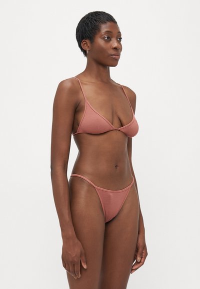 Kobieta w prążkowanym, kurzowym różowym bikini, stojąca pod kątem w lewo na jednolitym białym tle.
