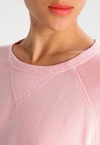 Helles rosa Sweatshirt mit einem gerippten Kragen, das aus einem strukturierten Stoff besteht und sichtbare Nähte aufweist, die das sportliche Design betonen.