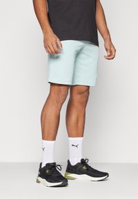 Calções azul claros feitos de tecido suave, combinados com sapatilhas de desporto pretas, meias brancas com logotipo preto e uma t-shirt escura.