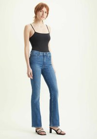 Jeans a vita alta in denim blu, realizzati in cotone, design a cinque tasche, leggera scoloritura, abbinati a una canotta nera aderente e tacchi a strappo.