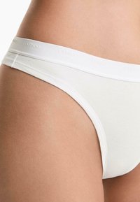 Close-up van witte damesondergoed met een zachte tailleband waarop "OYSHO" is gebrandmer Mayk, dat de stofstructuur en pasvorm benadrukt.