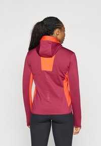 Aangesloten jack in diep bordeauxrood met contrasterende oranjepanelen, voorzien van een capuchon en textuurstof met branding op de onderrug.
