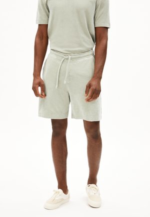 Shorts vert clair avec un cordon de serrage à la taille, fabriqués en tissu doux. Associés à un haut à manches courtes assorti et des baskets claires.