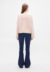 Πουλόβερ με ροζ και μπεζ ρίγες και ριμπ στο τελείωμα, σε συνδυασμό με σκούρο μπλε καμπάνες τζιν. Το πουλόβερ έχει ριγμένους ώμους και ετικέτα στην πλάτη.