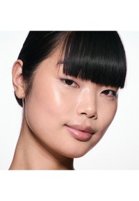 Portrait d'une personne au teint lisse et clair, cheveux noirs stylisés en frange droite, et lèvres pulpeuses, sur fond blanc.