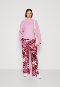 Rosa oversized tröja, blommönstrade vida byxor i rosa och krämfärg, matchat med vita sneakers. Enkel tote-väska över axeln.
