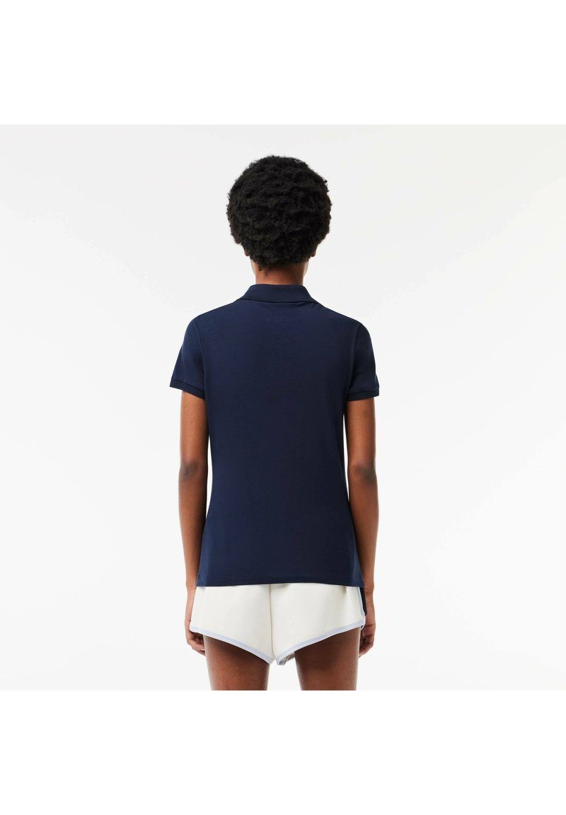 Navyblauwe polo met een kort mouw ontwerp, met een klassieke kraag en een rechte zoom aan de achterkant, gedragen met lichtgekleurde shorts.
