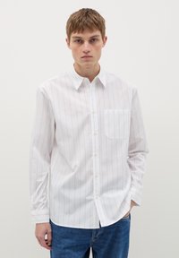Witte langemouw shirt met dunne verticale blauwe strepen, button-down kraag, enkele borstzak en een rechte pasvorm, gedragen met blauwe jeans.
