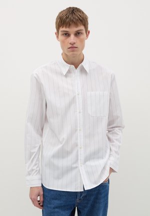 White long-sleeve shirt with thin vertical blue stripes, button-down collar, single chest pocket, and a straight fit, worn with blue jeans.