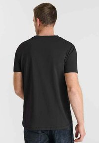 T-shirt nera a maniche corte esposta dal retro. Tessuto in cotone liscio con scollo rotondo classico e design semplice.