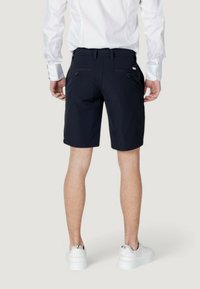 Pantaloni corti blu scuro con frontale piatto, due tasche posteriori e passanti per cintura. Abbinati a una camicia bianca a maniche lunghe e scarpe da ginnastica bianche.