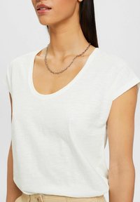 Biała krótko-sleeve t-shirt z głębokim dekoltem w serek, wykonana z lekkiego materiału, w połączeniu z srebrnym naszyjnikiem.