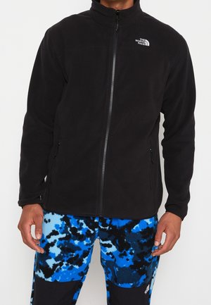 Homme portant une veste polaire noire zippée avec le logo The North Face et un pantalon à motifs bleus, noirs et blancs.