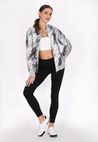 Jachetă bomber abstractă cu model gri și negru, top scurt alb, colanți negri și adidași albi. Material neted cu manșete elastice.