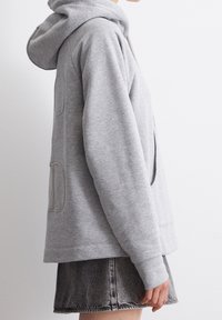 Sudadera gris clara hecha de una tela suave con un bolsillo tipo canguro y puños acanalados. Cuenta con una capucha con cordón y un diseño de corte relajado.
