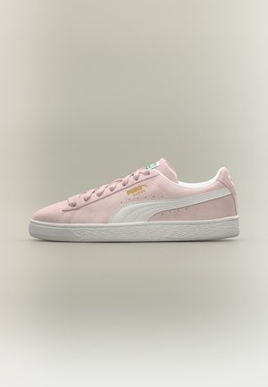Ροζ sneaker Puma με κατώτερο μέρος από σουέντ, λευκή ρίγα, λευκή σόλα και χρυσό λογότυπο Puma Suede στο πλάι σε ουδέτερο φόντο.