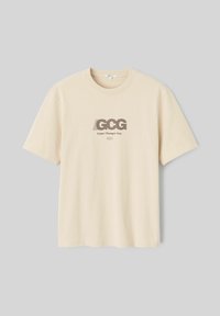 T-shirt en coton beige à manches courtes, avec un motif imprimé "GCG" et "Game Changer Guy" en marron, centré sur le devant.