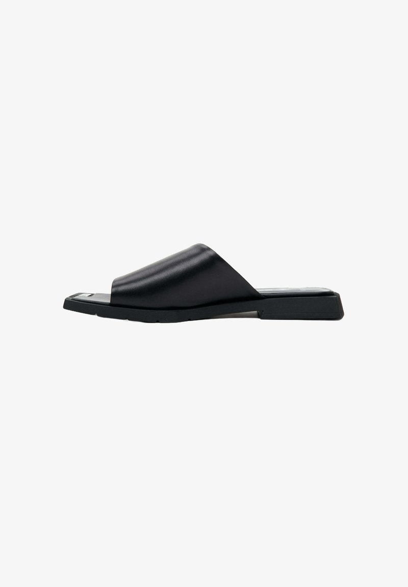 Black leather slide sandal featuring a wide upper strap, flat sole, and minimalist design. Smooth texture with a slightly curved shape.