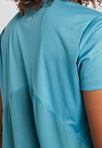 Turkosidrottströja med slätt tyg och meshpaneler. Har en Nike-logotyp på övre delen av ryggen, korta ärmar och en avslappnad passform.