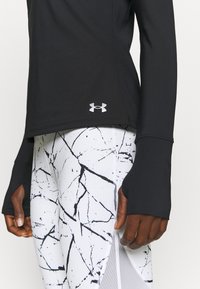 Svart långärmad träningströja med tumhål, i kombination med vita leggings med svarta abstrakta mönster. Båda är tillverkade av töjbar tyg.