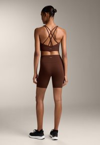 Barna aktív sportöltözet szett, keresztpántos sportmelltartóval és magas derekú biciklis rövidnadrággal. Simább textúra, testhezálló kialakítás és minimális márkázás.