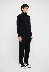 Black knit turtleneck sweater and matching joggers with a drawstring waist. Paired with black and white sneakers, featuring a sleek design.