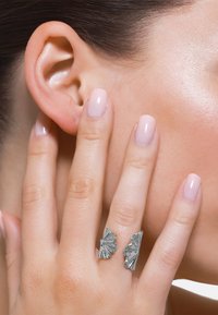 Sterling sølv ring med en bølgete, teksturert design. Ringen vikler seg rundt to fingre og har en polert overflate. Neglene er manikyrert.