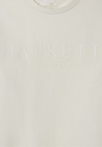 Krémovohnedá tkanina s embosovaným textom "HACKETT LONDON" umiestneným v strede pod okrúhlym výstrihom.