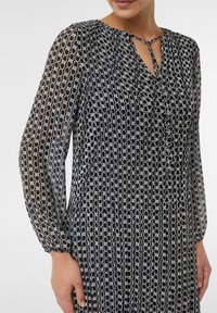 Zwart-witte blouse met een kettinglinkpatroon, met lange mouwen, een ronde hals met een strikdetail en een geraffineerde textuur.