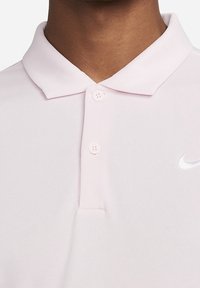 Ljusrosa polo skjorta i mjukt tyg, med en klassisk krage, två knappar och en liten vit Nike-logotyp på övre vänstra sidan.