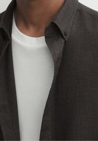 Czarna szara koszula zapinana na guziki nałożona na gładki biały T-shirt. Materiał wydaje się mieć strukturę, z wyraźnym kołnierzykiem i detalami guzików.