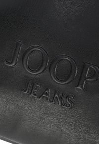 Čierna kožená kabelka s debossovaným logom "JOOP JEANS", textúrovaným povrchom a hladkým finishom. Kompaktný dizajn s zaoblenými hranami.