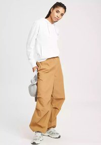 Biała bluza z kapturem, luźne beżowe spodnie i szara torba na ramię; trampki mają fakturowany wzór; swobodny krój i casualowy styl.