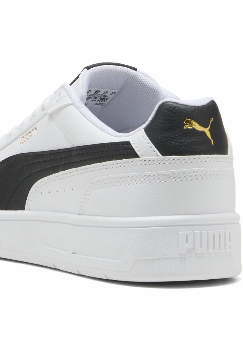 Schwarz-weiße Sneaker aus Leder und synthetischen Materialien, mit einem strukturierten schwarzen Streifen, goldenen Akzenten und einer robusten weißen Sohle.