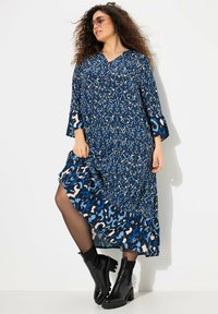 Blå mönstrad maxiklänning med ¾ ärmar, med en v-ringning och sidoklyvning. Bärs med svarta ankelstövlar. Slät textur och flödande design.