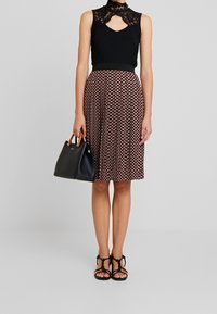 Schwarzes ärmelloses Top mit Spitzenkragen, gemusterter Midirock in Kastanienbraun und Creme, schwarze Handtasche und schwarze Sandalen mit Riemchen.