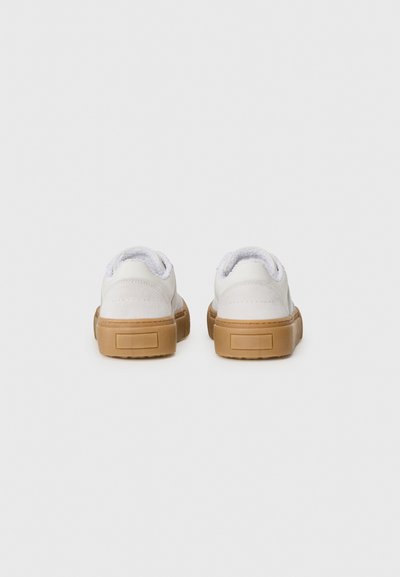 Vita mocka sneakers med låg tå, som har en mjuk innersula, en tan gummisula och minimalistisk design. Inga synliga mönster eller detaljer.