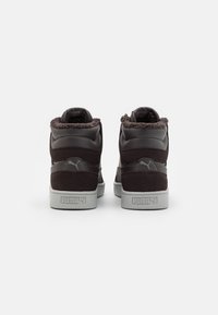 Czarne sneakersy typu high-top z teksturowaną syntetyczną cholewą, futrzanym kołnierzem wokół kostki i szarej gumowej podeszwie. Charakteryzują się wyraźnym logo Pumy na pięcie.